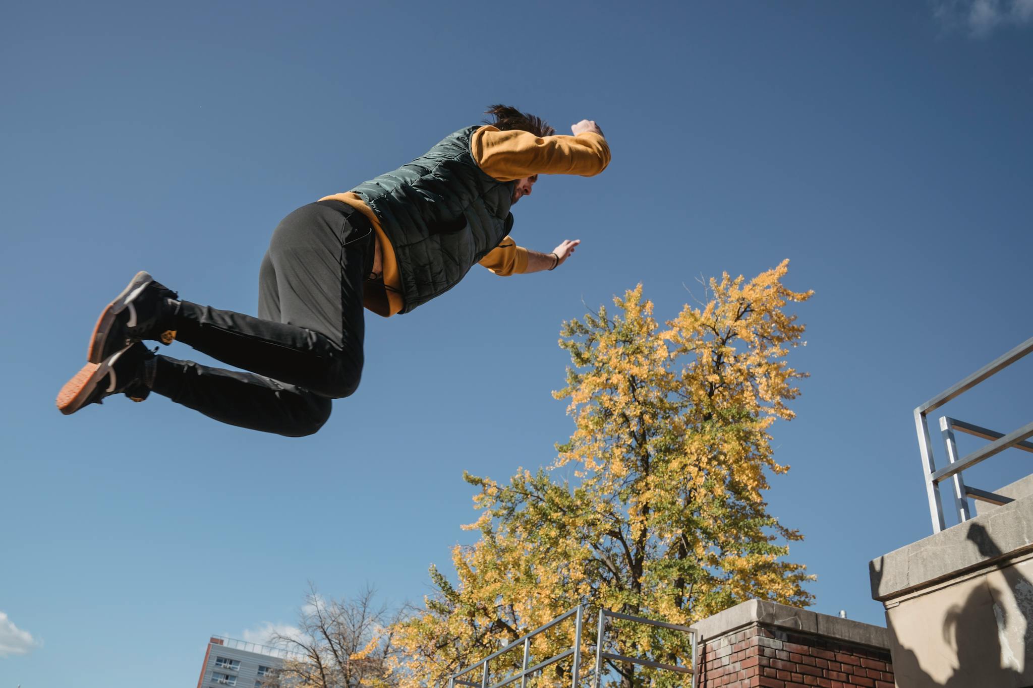 A man performing a parkour jump against a clear blue sky in an urban setting.