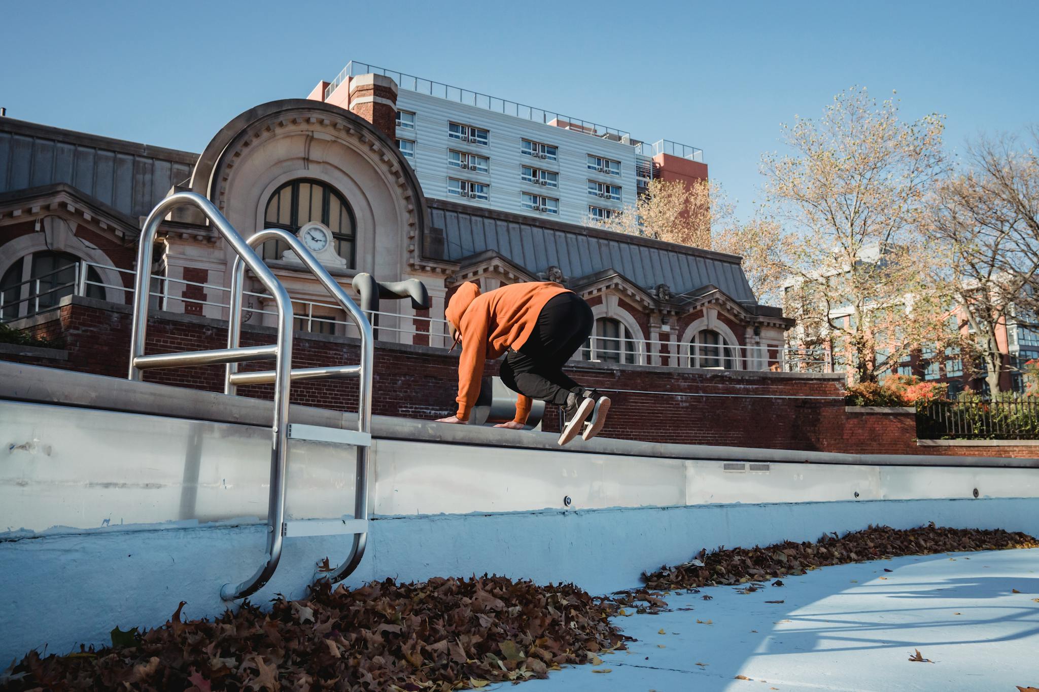 An athletic man performs parkour tricks in an empty pool area near a historic building.