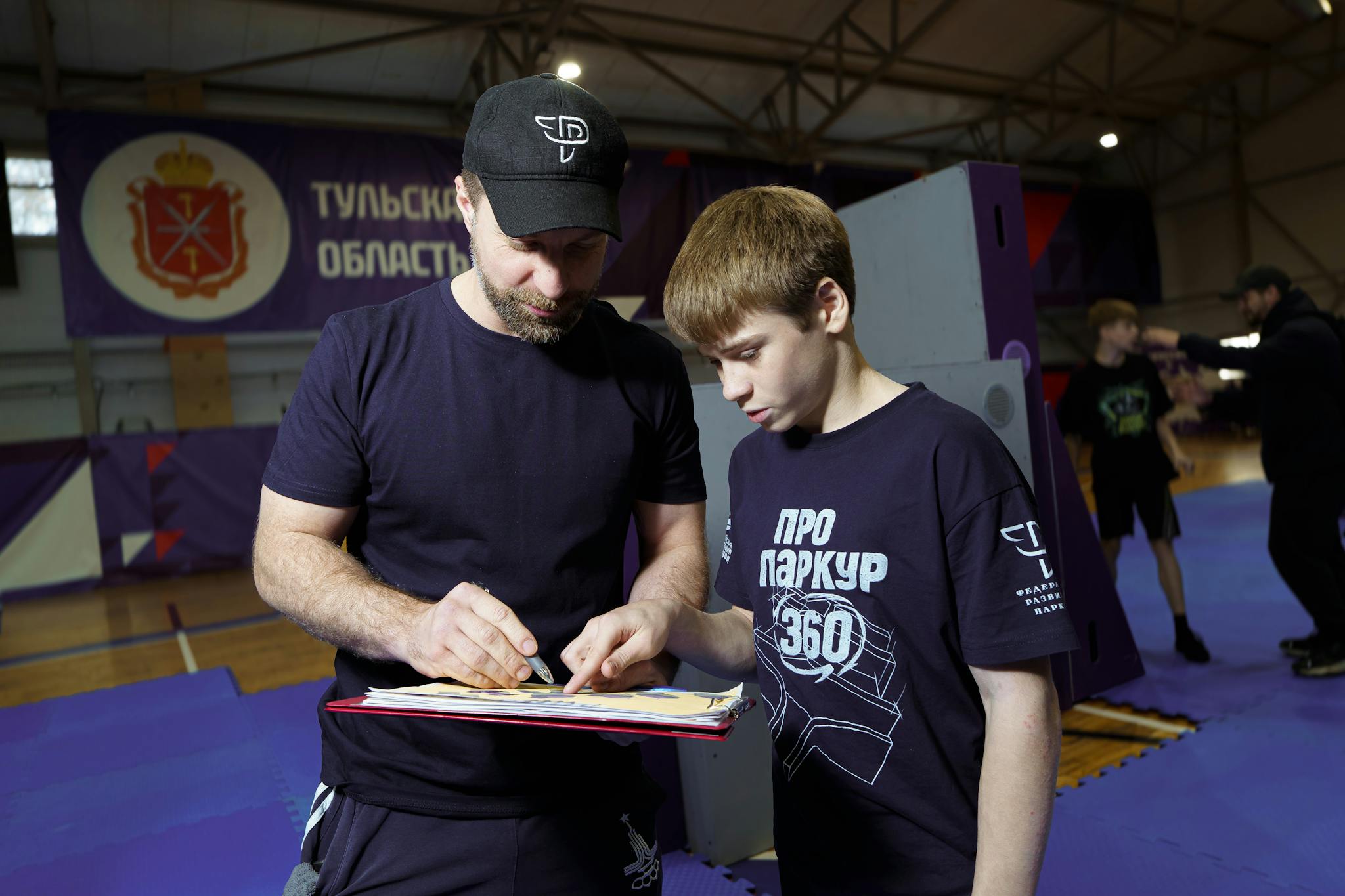 Instructor and teenager reviewing parkour moves at an indoor gym.