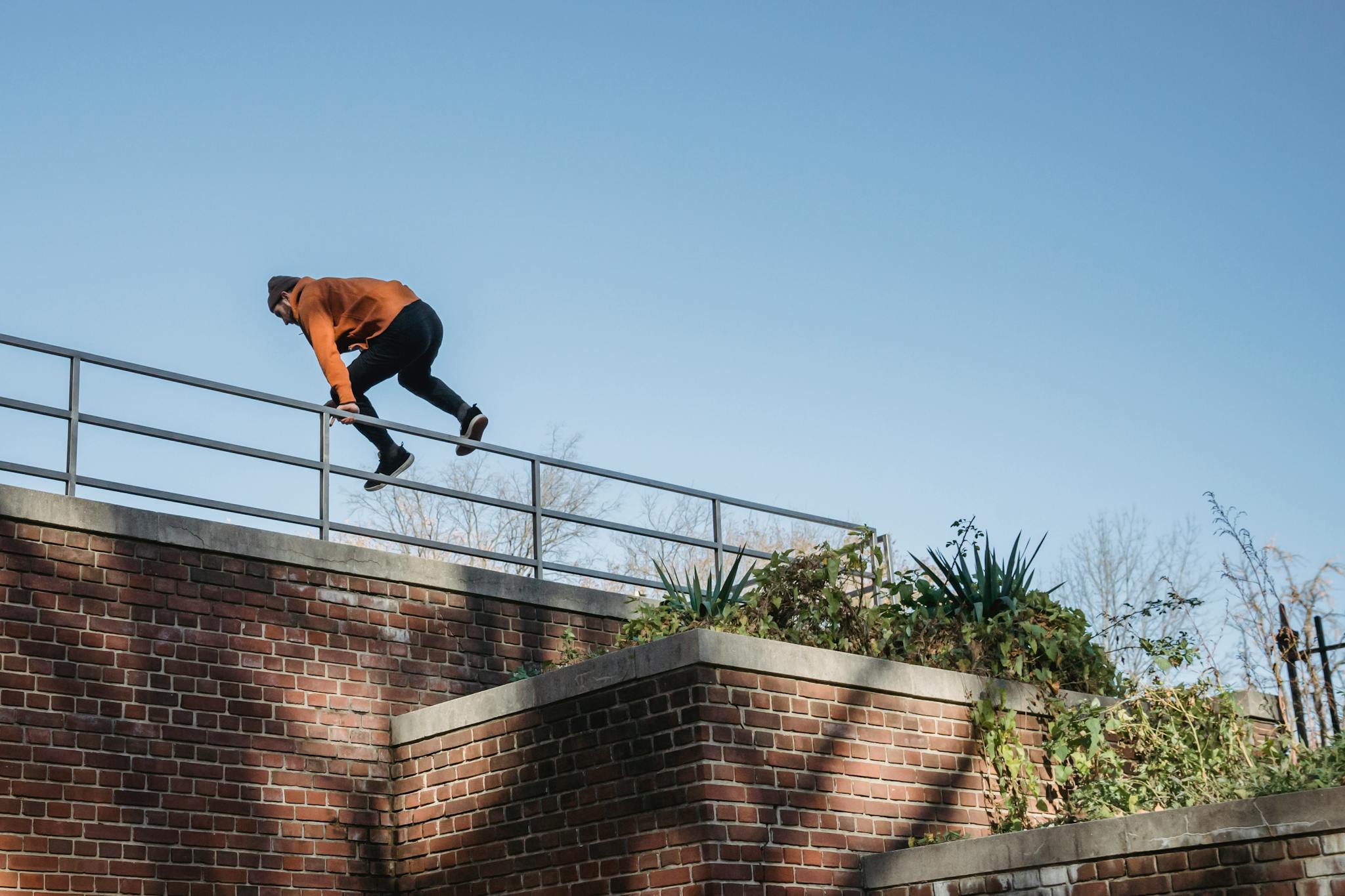 Man performing a parkour jump over a brick wall under a clear blue sky, showcasing agility and freedom.