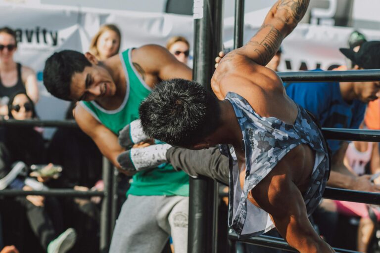 Two men working out on a pull-up bar during a daytime outdoor fitness event.