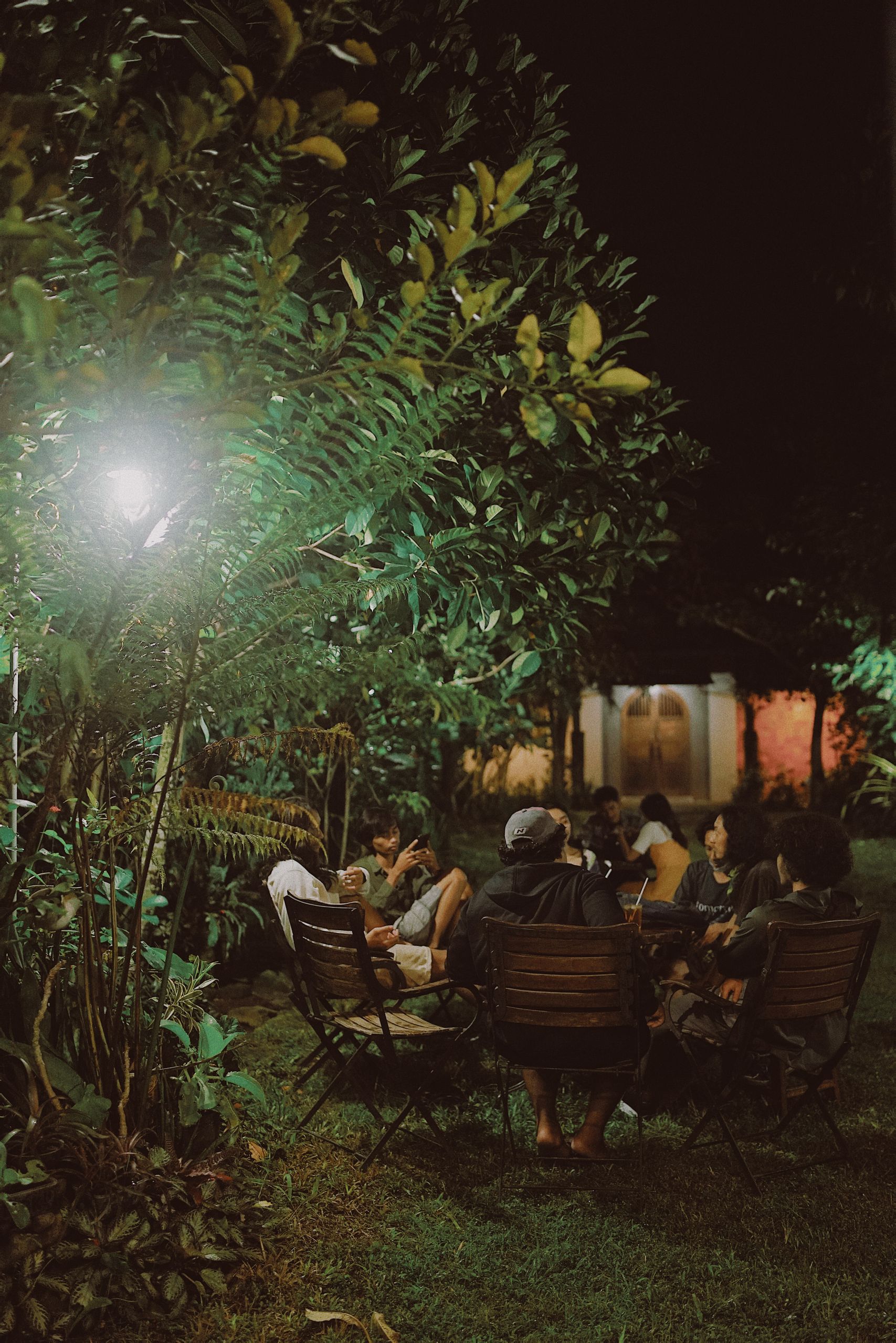A group of adults enjoying a nighttime gathering in a garden with ambient lighting.