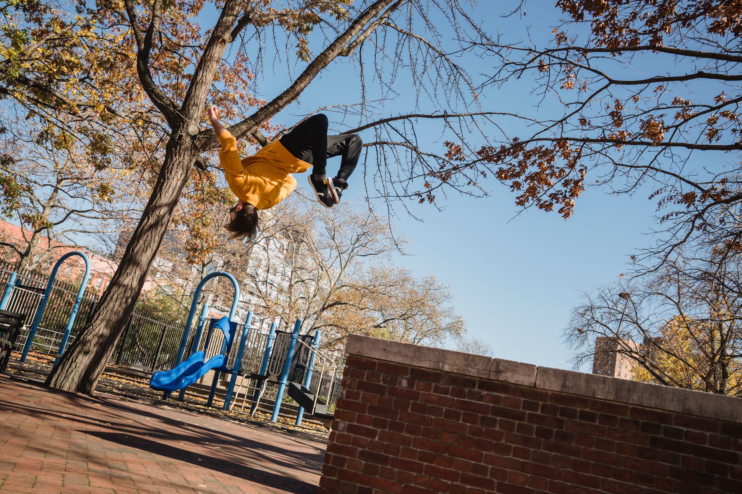 From below full length of faceless young male wearing casual clothes and jumping from fence while doing parkour stunts in city street in autumn day
