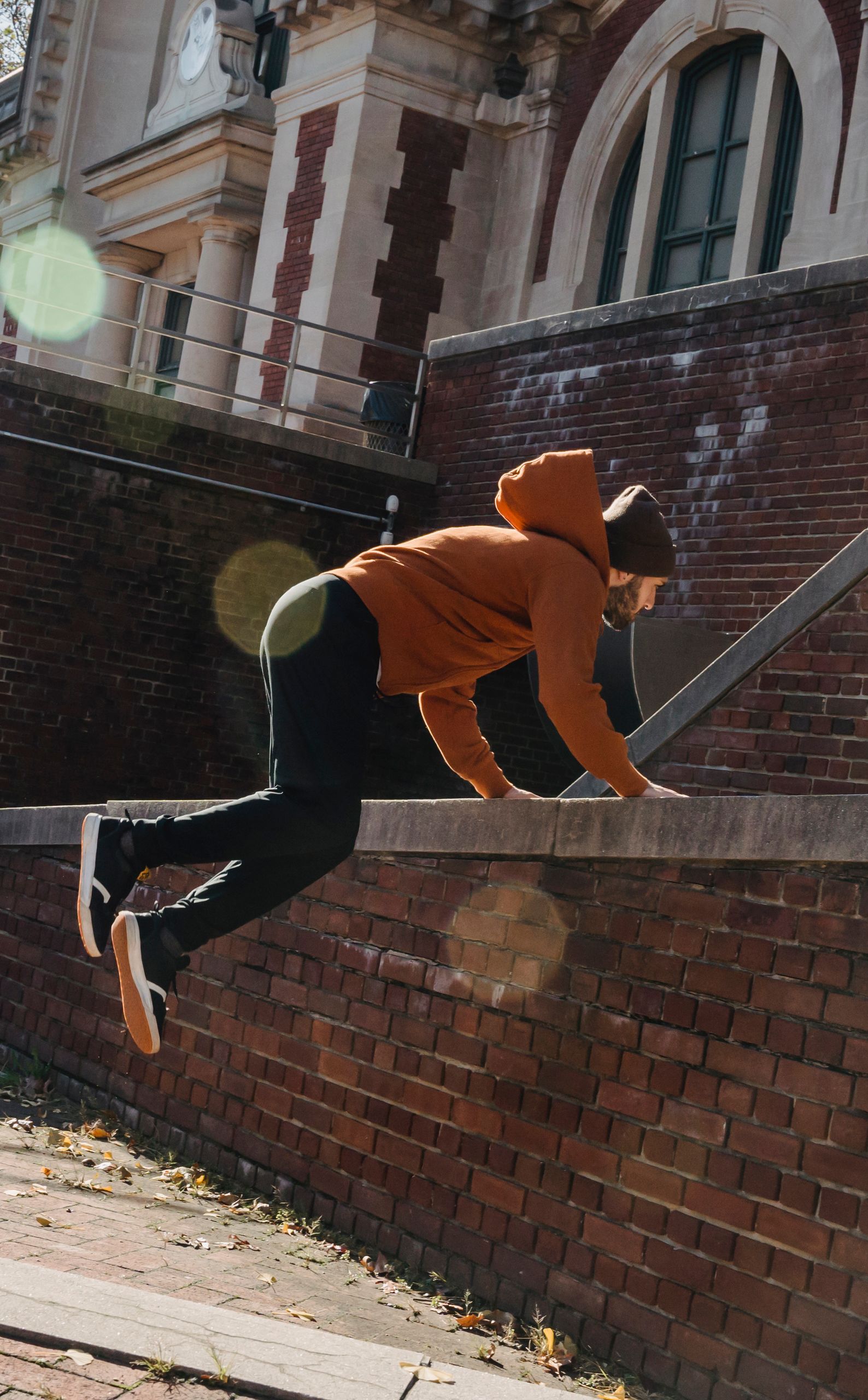 Full body side view of agile male in hat jumping over brick border against aged building on street during exercise